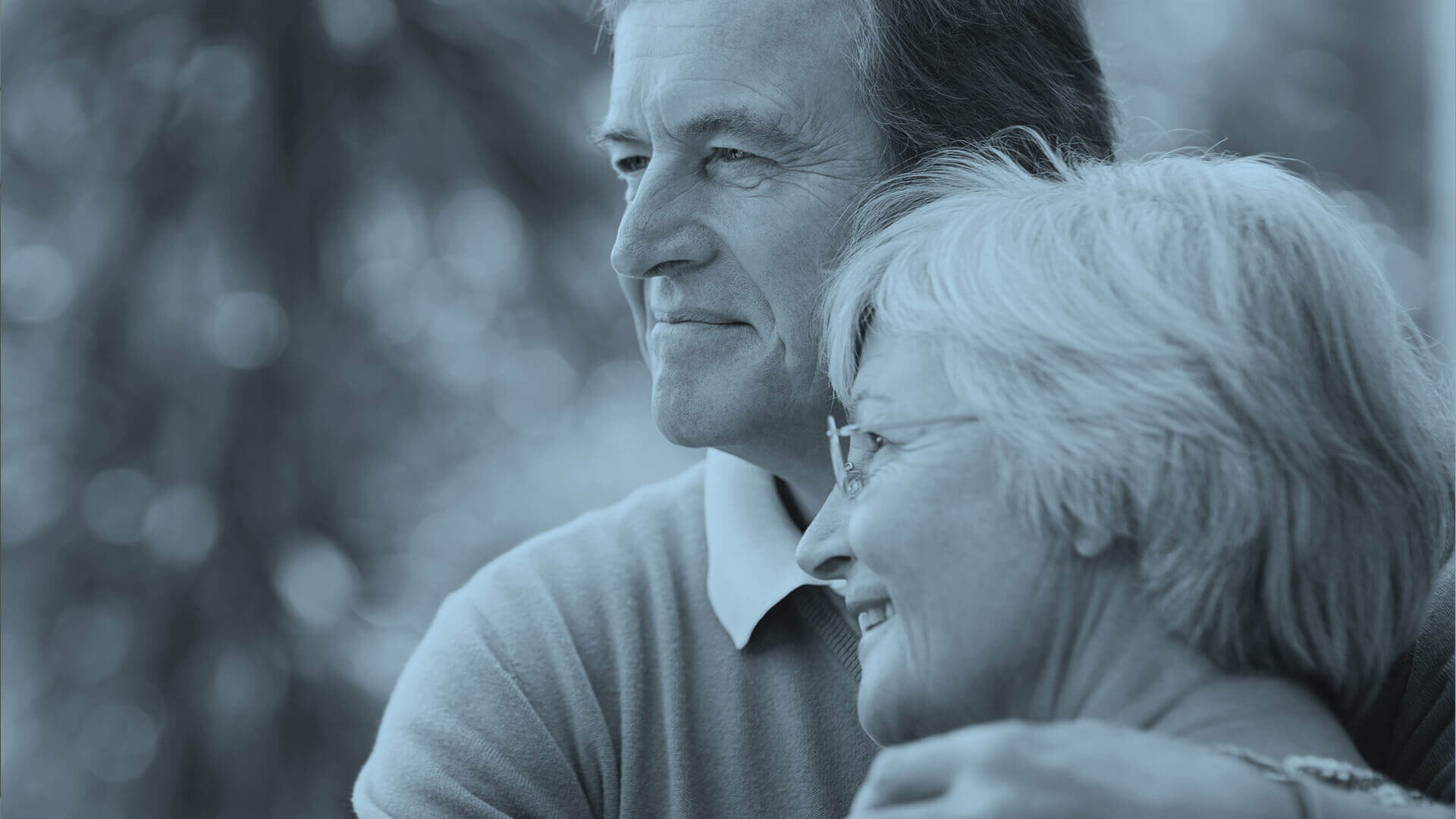 Couple in their sixties or seventies with white hair holding each other looking joyful